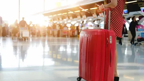 Ταξιδιώτισσα σε αεροδρόμιο με κόκκινη βαλίτσα